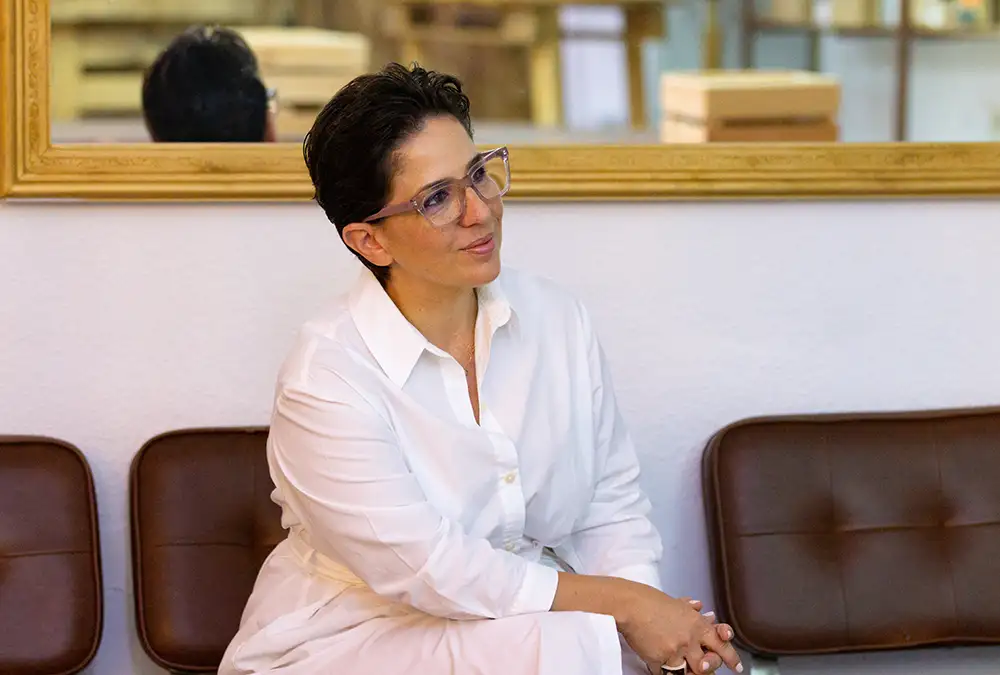 Susi Boix con camisa blanca y gafas transparentes mirando hacia un lado y sonriendo suavemente.